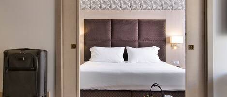 Una habitación de hotel con una cama, una maleta, un bolso y una mesa.