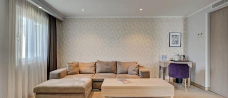A modern living room with a beige sectional sofa, a wooden coffee table, and a small desk with a purple chair.