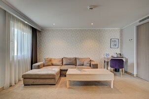 Een moderne woonkamer met een beigekleurse modulaire bank, een houten salontafel en een bureau met een paarse stoel.