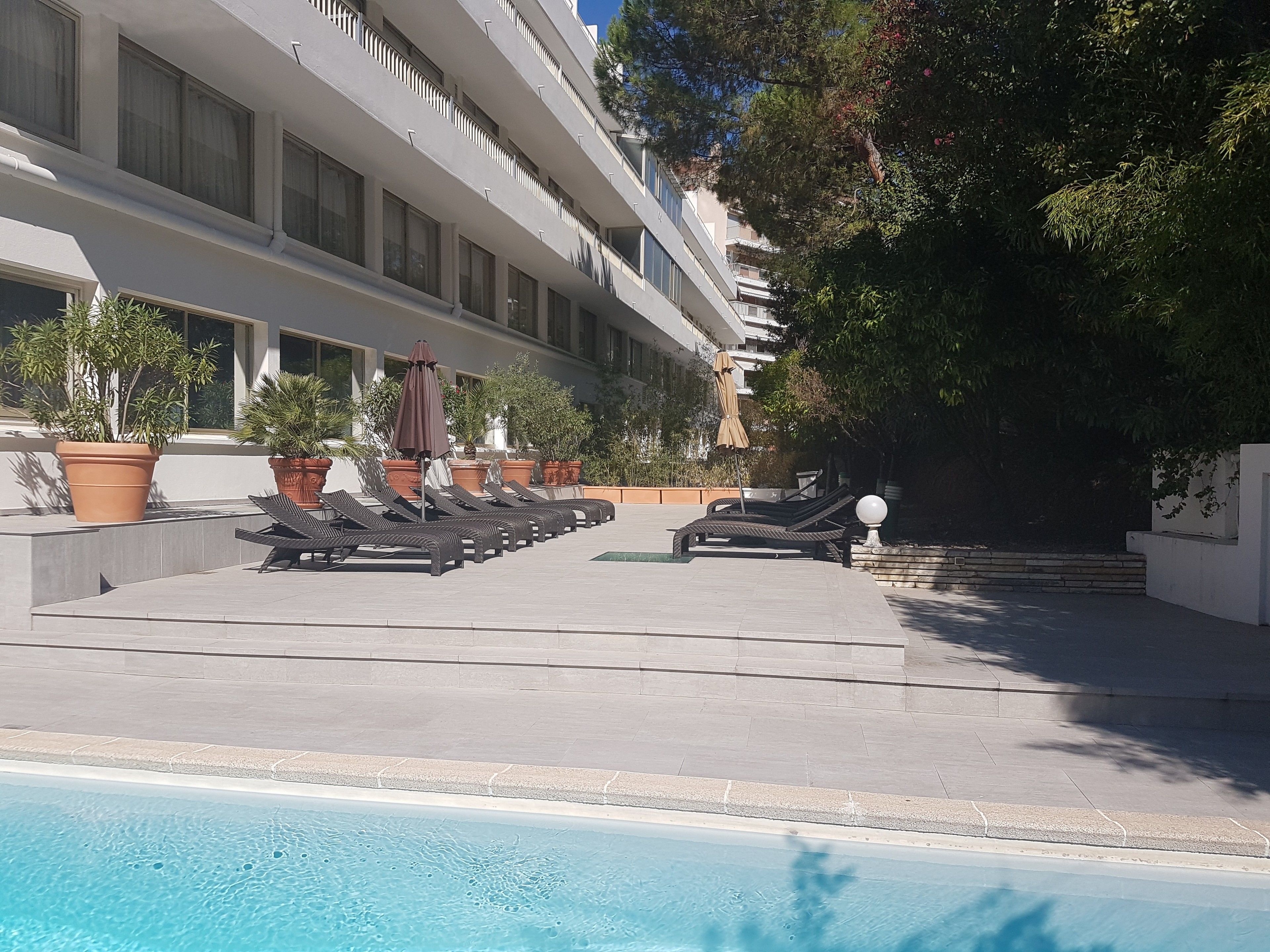 A hotel with a pool area, sun loungers, and potted plants.