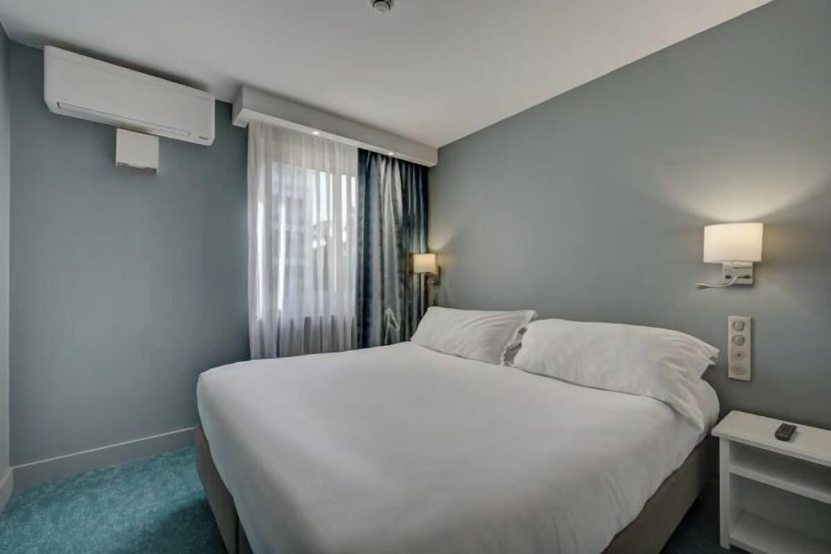 A hotel room with a bed, a nightstand, a lamp, and an air conditioning unit.