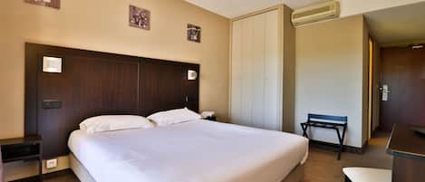 A hotel room with a large bed, a desk, a chair, and a wardrobe.