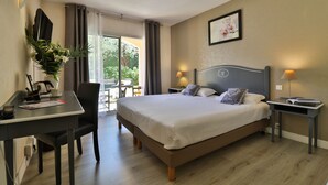 A hotel room with a bed, desk, chair, and a view of greenery outside. - Le Floréal (Vence)