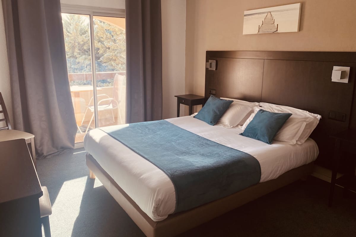 Une chambre d’hôtel avec un grand lit, un petit bureau et une vue sur l’extérieur grâce à une porte coulissante.