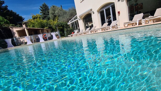A clear swimming pool with lounge chairs and a building in the background. - Le Floréal (Vence)