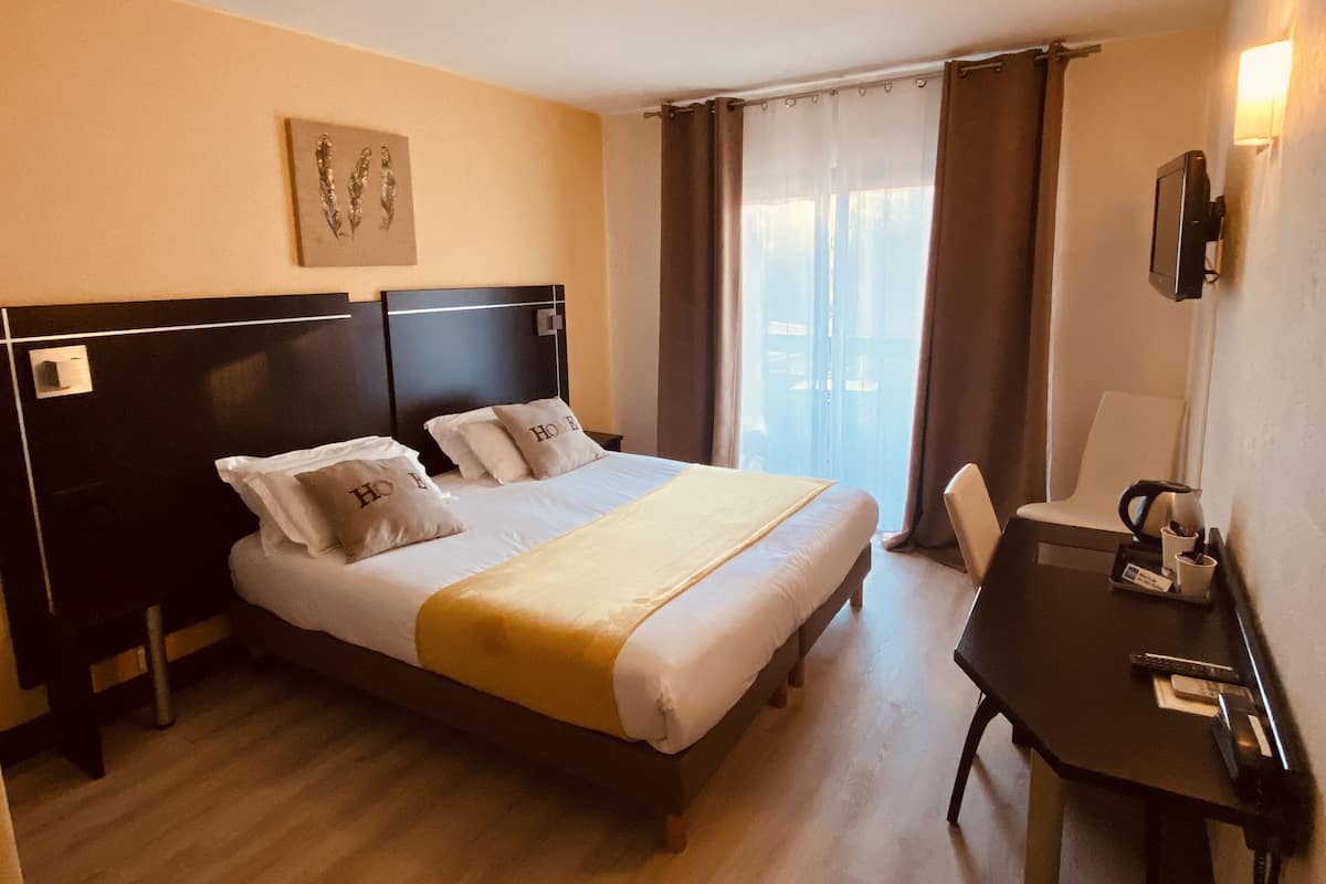 Une chambre d’hôtel équipée d’un lit, d’un bureau, d’une chaise, d’une télévision et d’une fenêtre avec des rideaux.