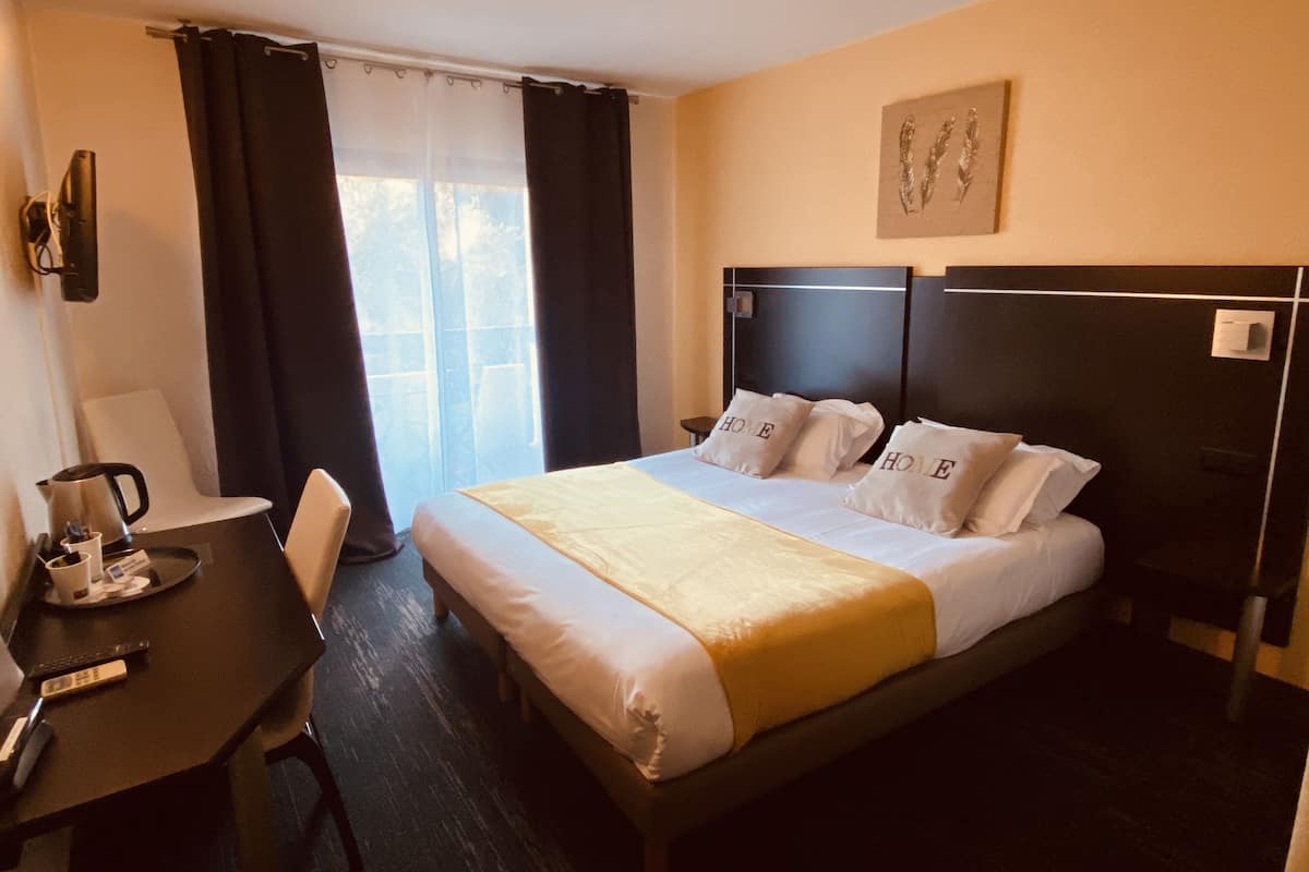 Une chambre d’hôtel comprenant un lit, un bureau avec une chaise, une machine à café et une fenêtre avec des rideaux.