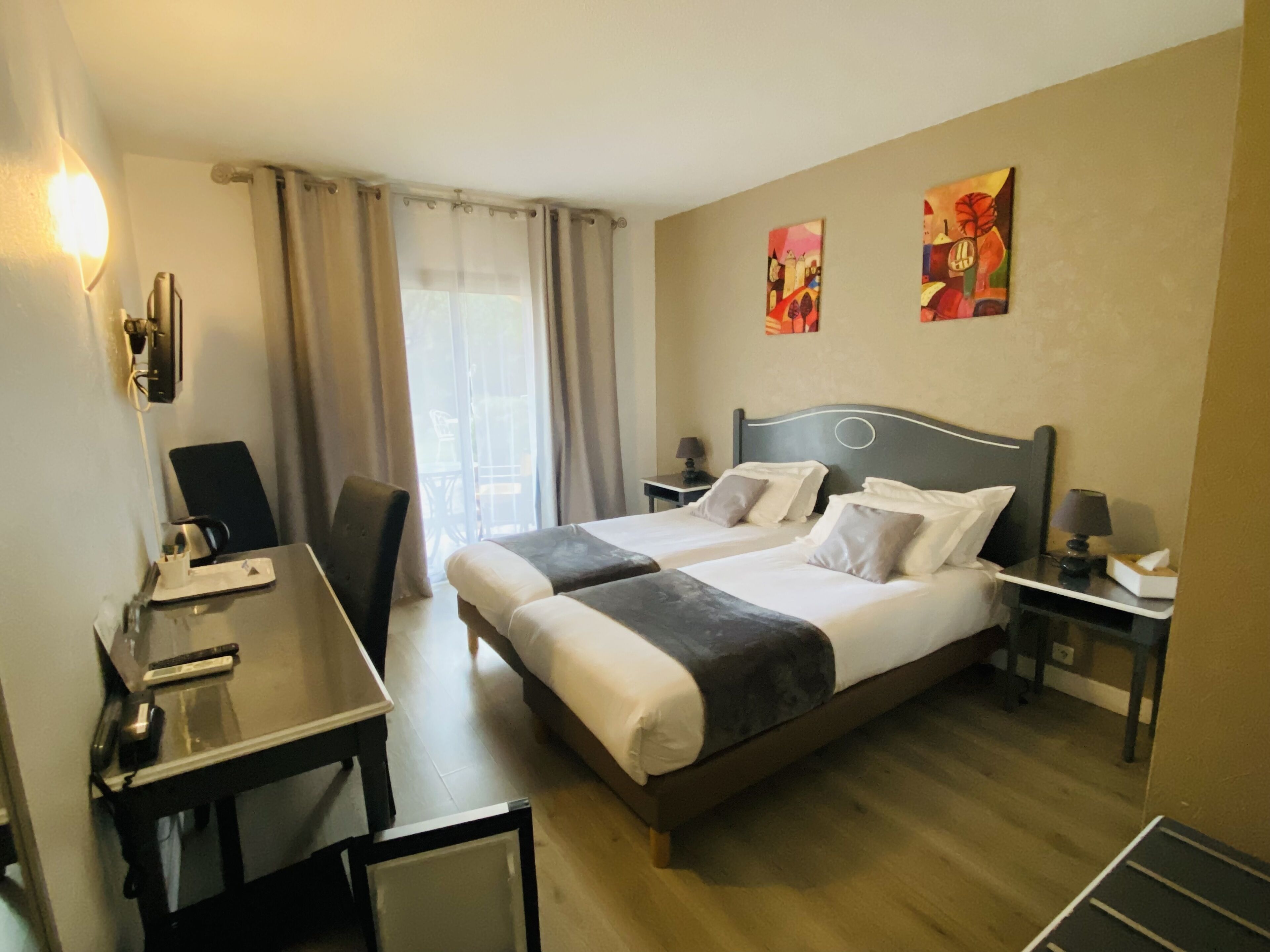 Habitación de hotel con dos camas, un escritorio, una silla, una lámpara y obras de arte en las paredes.