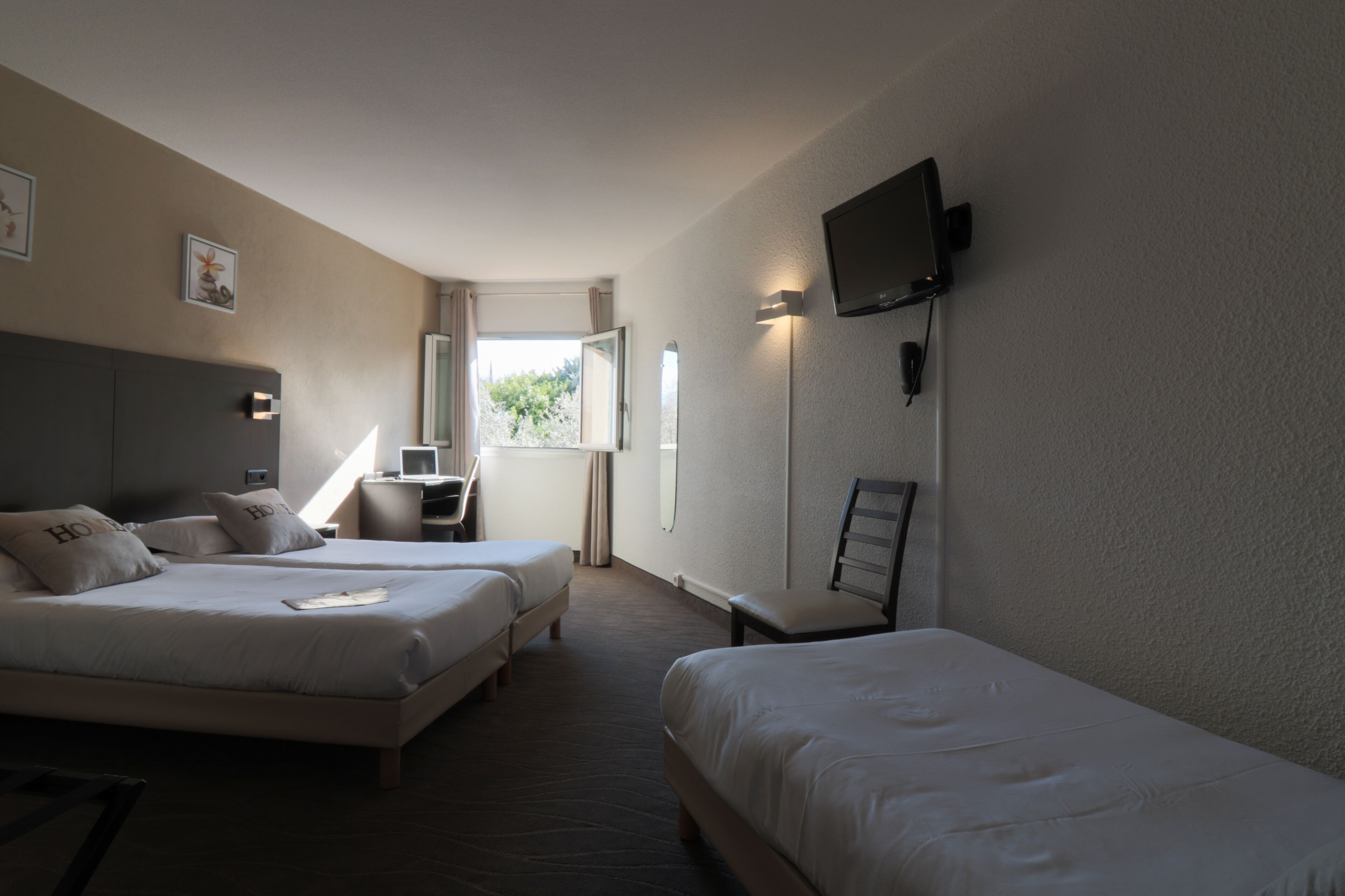 Habitación de hotel con dos camas, un escritorio, una silla, un televisor y un ventanal con cortinas.