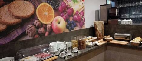 Um buffet de café da manhã com diversos alimentos e um grande mural de frutas e nozes na parede.