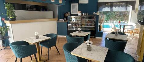 A restaurant with teal chairs and marble tables, a counter with a menu, and a view of an outdoor pool area.