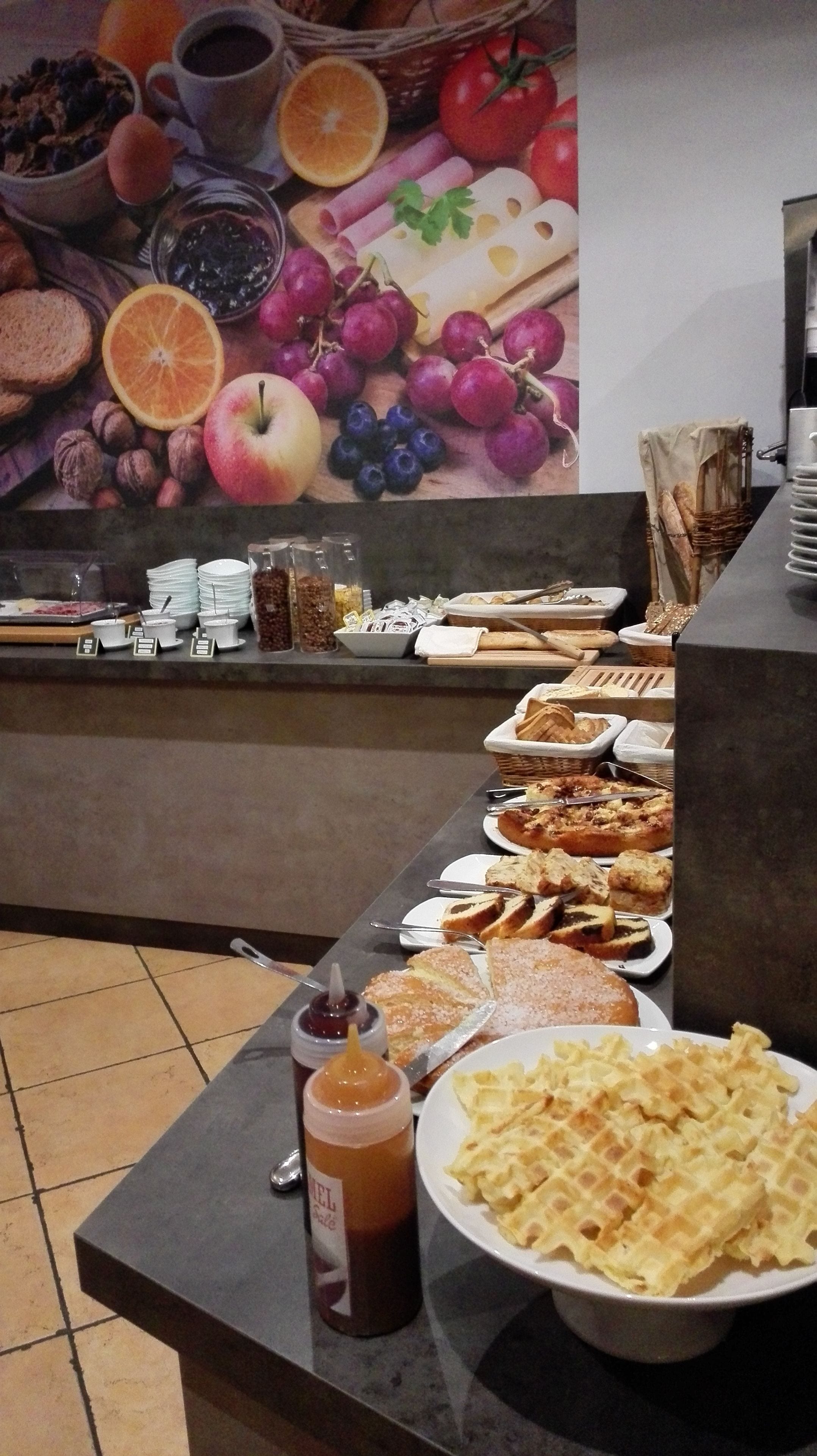 Un buffet proposant une variété de plats, notamment des gaufres, des pâtisseries et une bouteille de sirop.