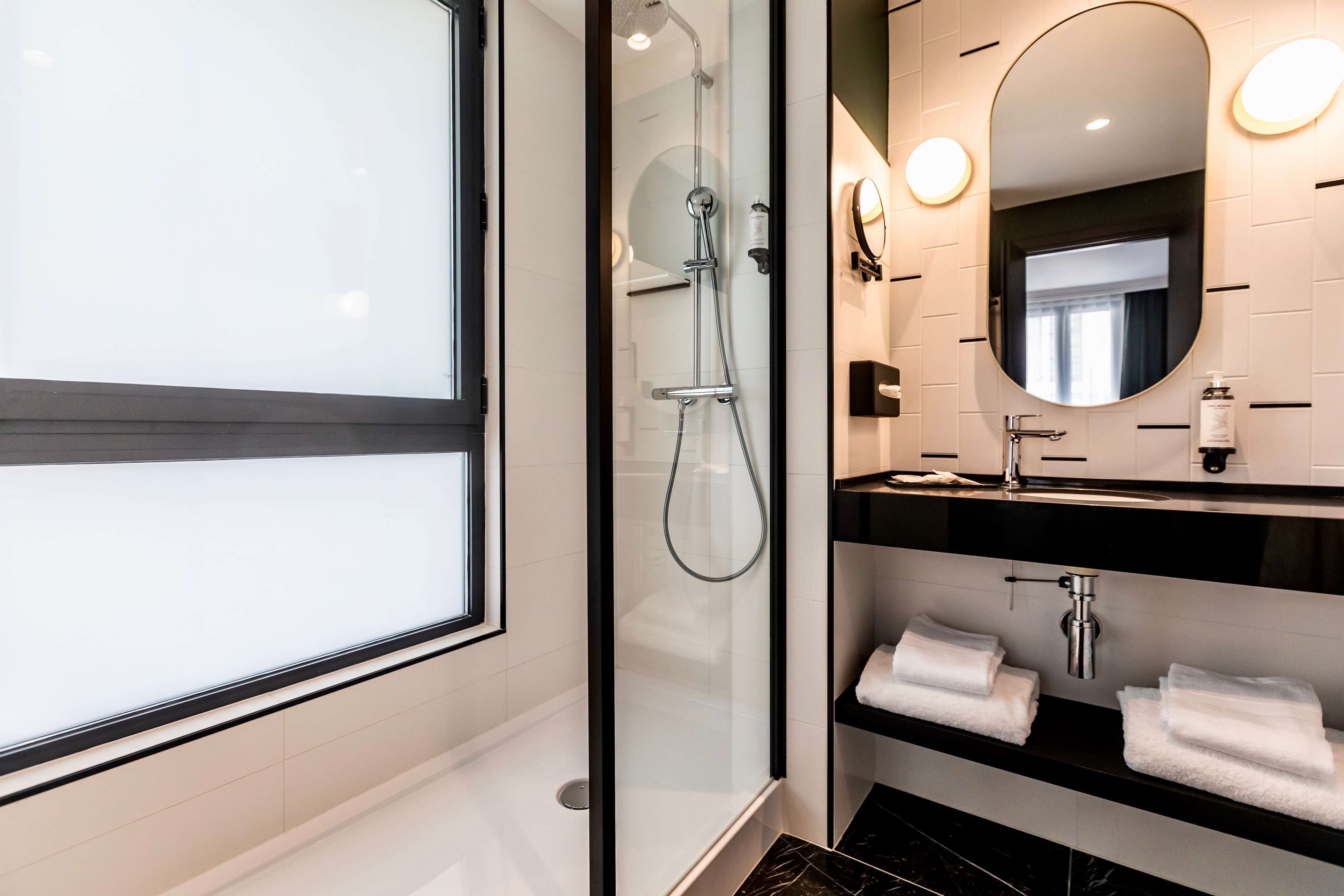 Un bagno moderno con cabina doccia in vetro, uno specchio grande e un piano lavabo nero con due asciugamani bianchi.