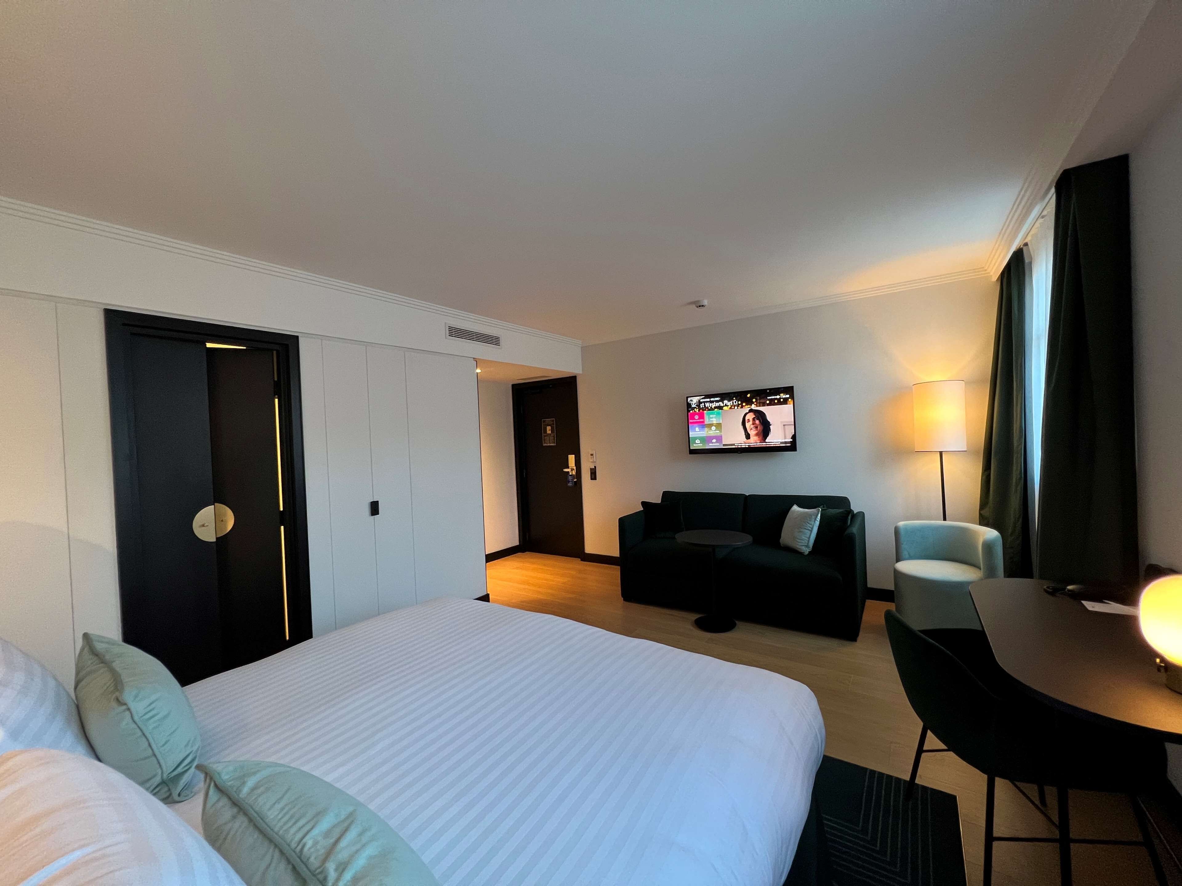 A hotel room with a large bed, a sofa, a TV, and a desk.