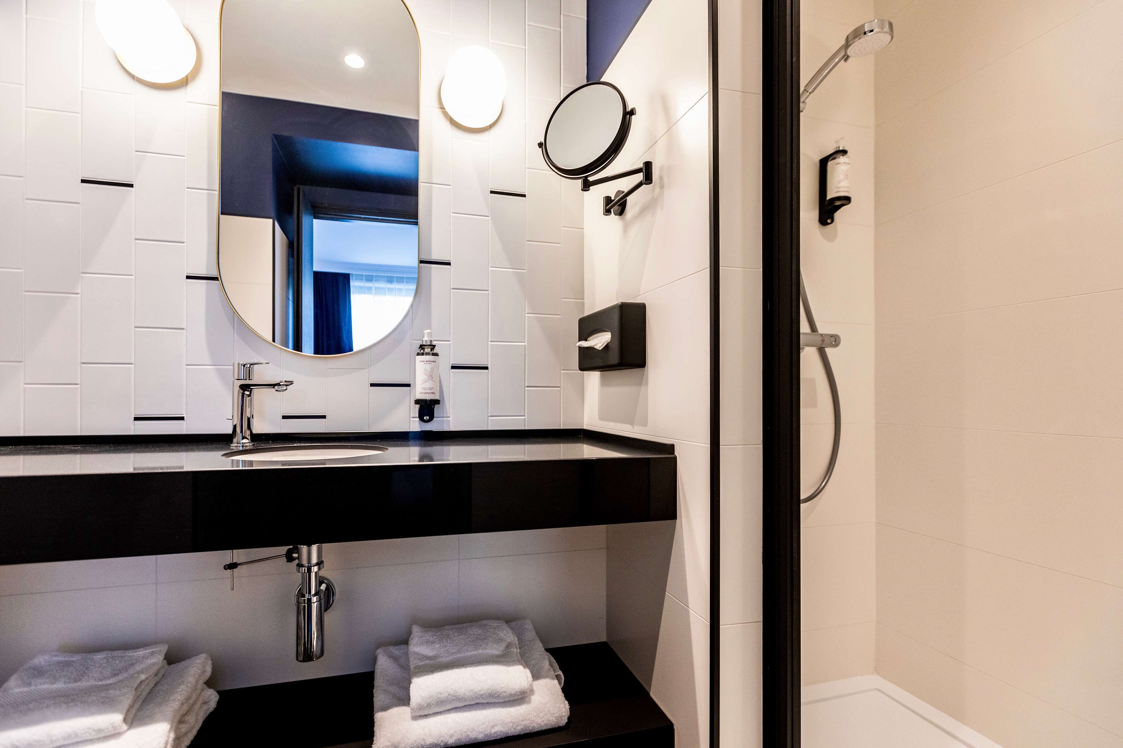 Um banheiro moderno com bancada preta, azulejos brancos, um espelho grande e área de chuveiro.
