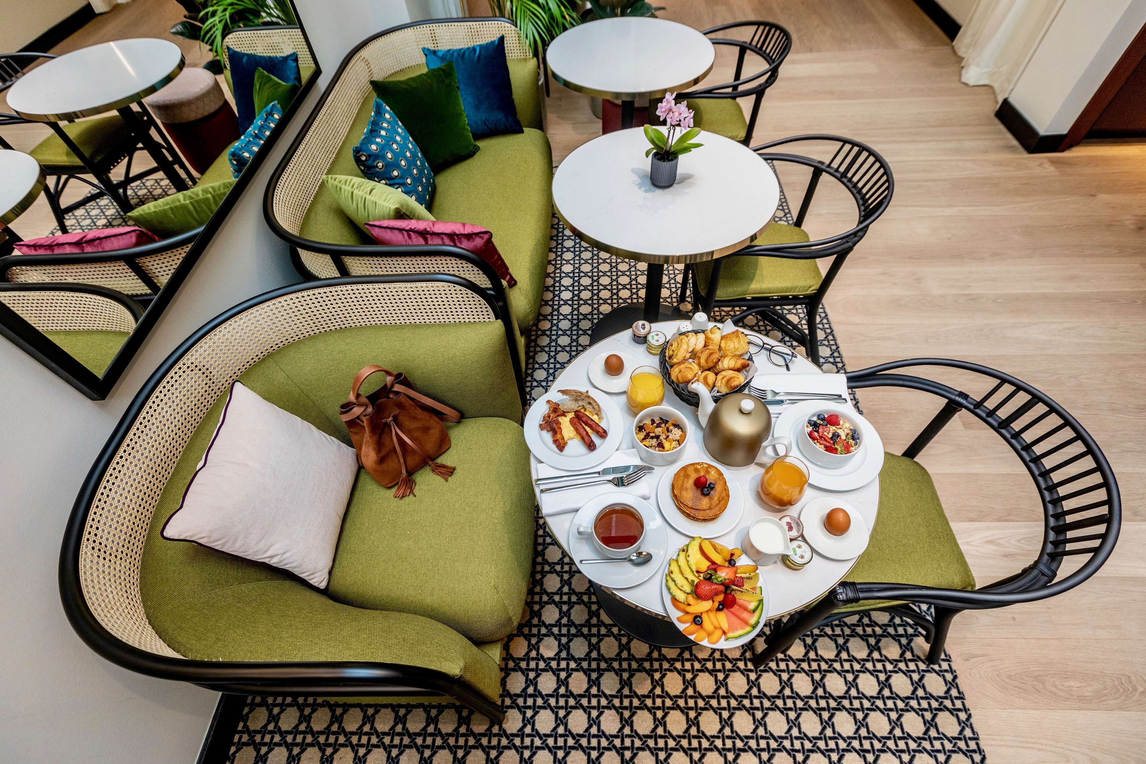 Un comedor con asientos acolchados verdes, mesas redondas y diversas opciones para el desayuno.
