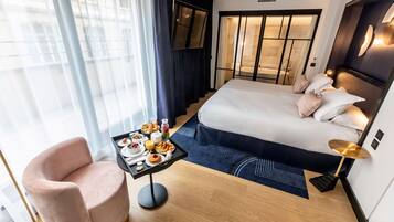 Habitación de hotel moderna con una cama grande, un escritorio con desayuno, una silla y vistas a la ciudad.
