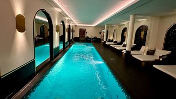 A long, narrow indoor pool with a blue water feature, surrounded by white seating areas and mirrored walls.