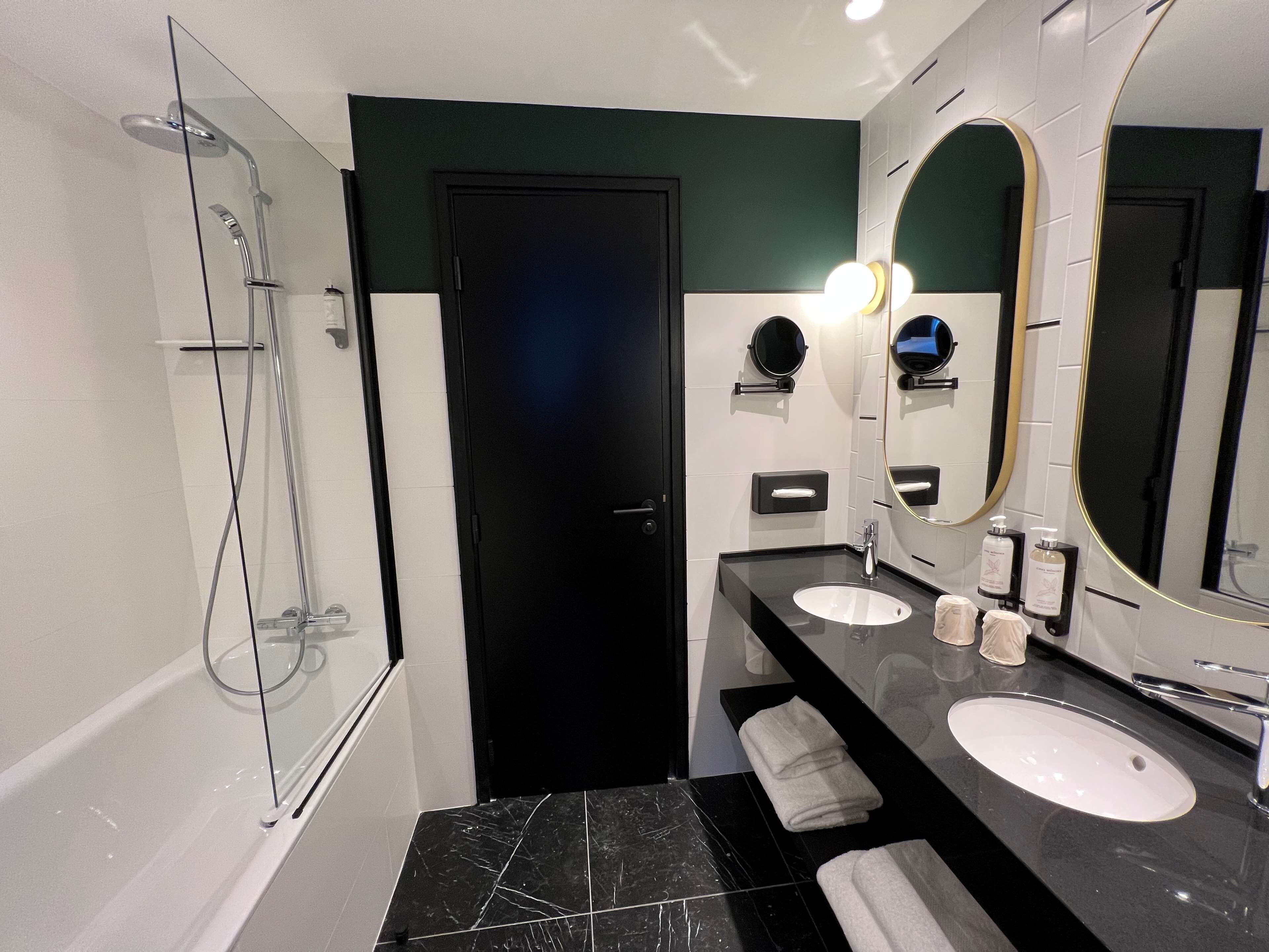 Un baño moderno con cabina de ducha de vidrio, dos lavamanos, un espejo grande y una puerta.