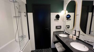 Un baño moderno con cabina de ducha de vidrio, dos lavamanos, un espejo grande y una puerta.