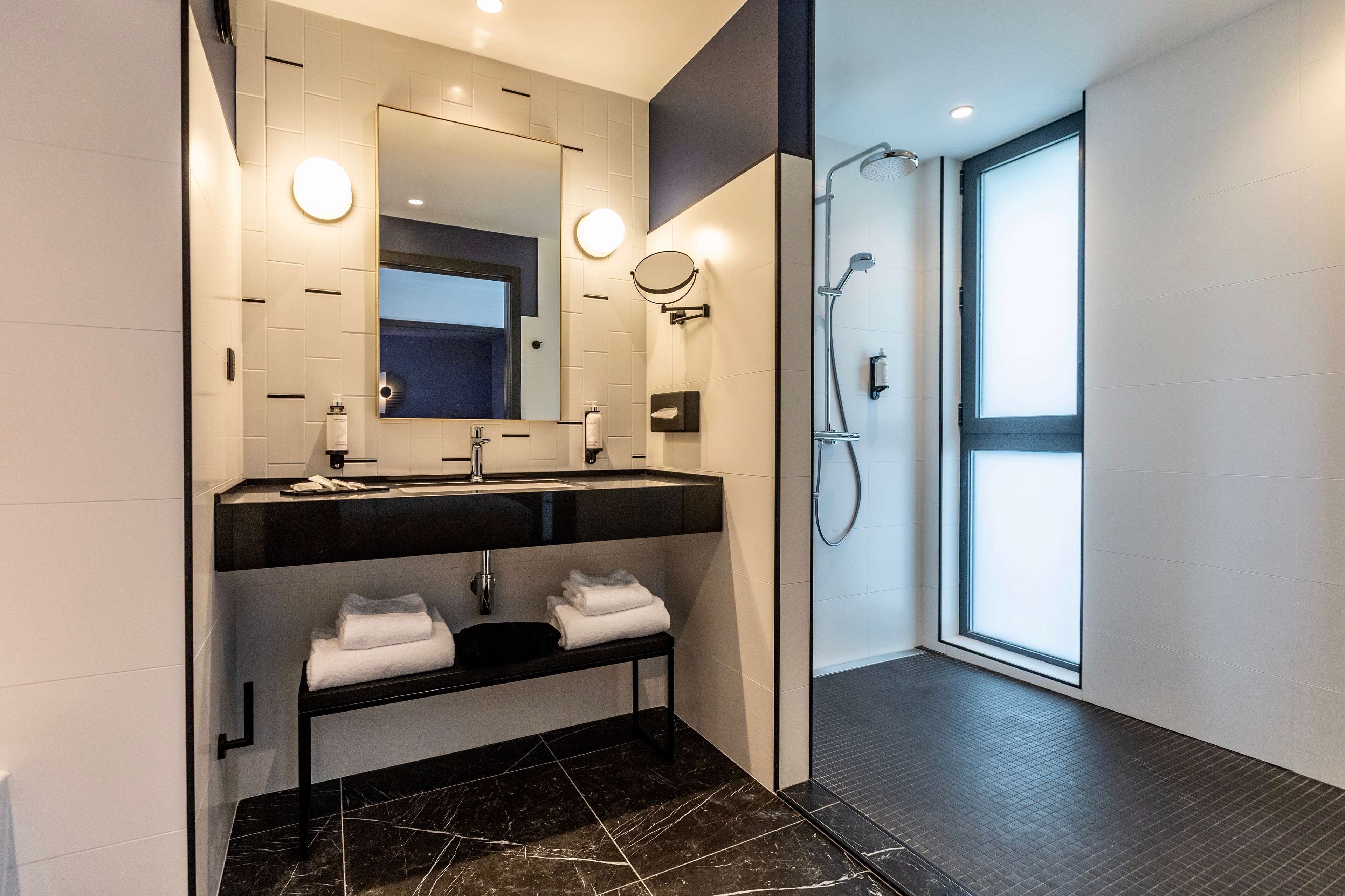 A modern bathroom with a black sink, white tiles, a large mirror, and a glass shower enclosure.