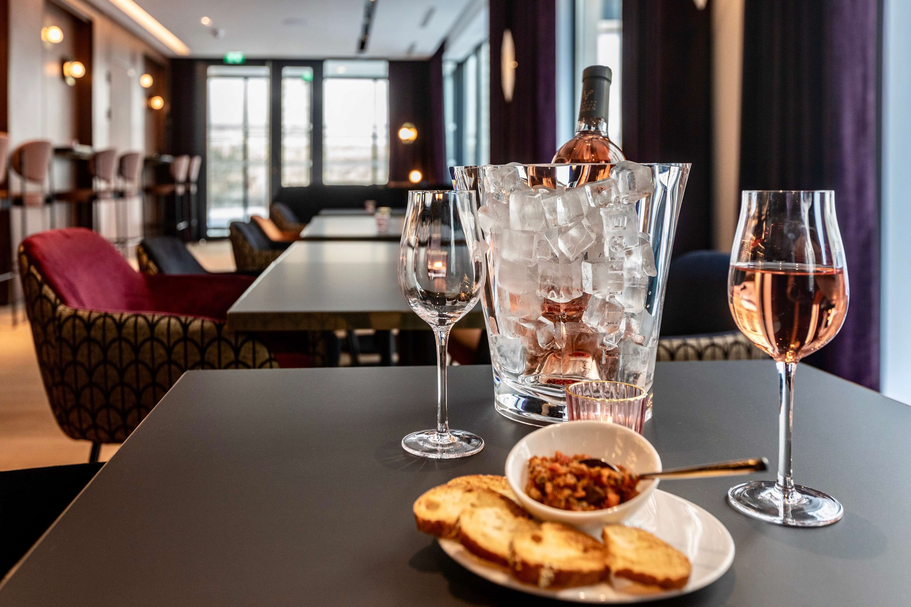 A dining table with a bottle of wine, two glasses, and a bowl of food.