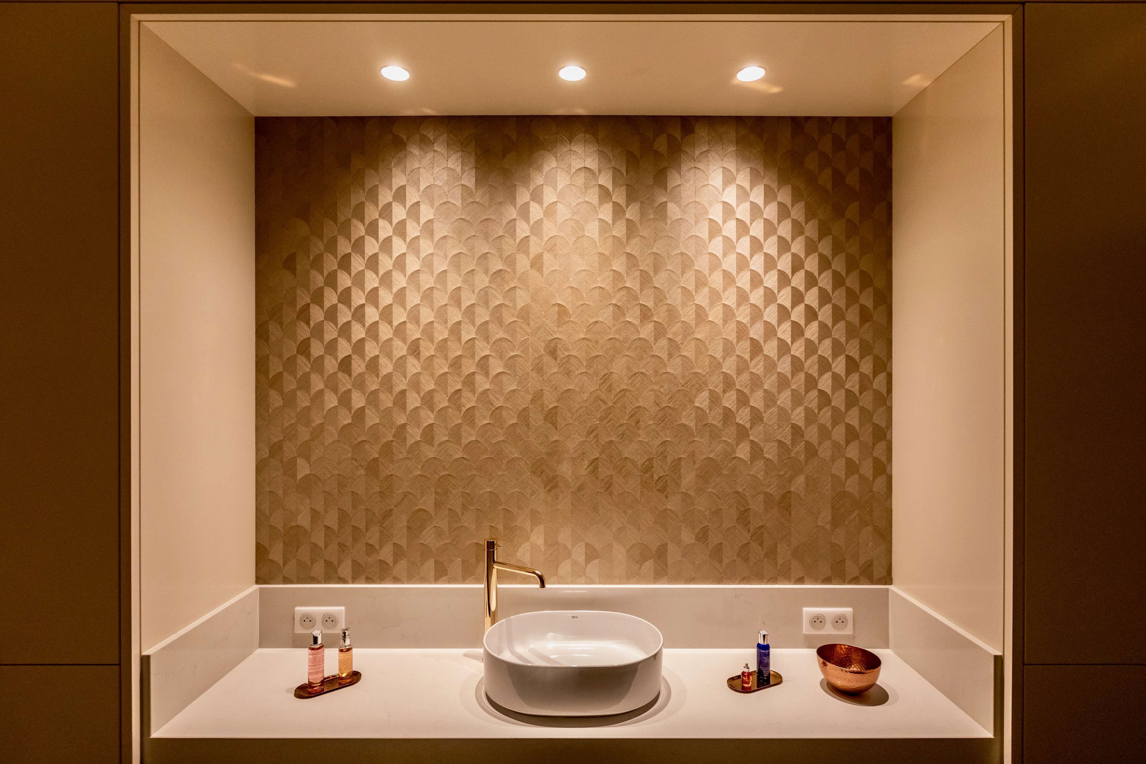 Une salle de bain moderne avec un mur orné d’un motif géométrique, un lavabo rond et deux robinets.