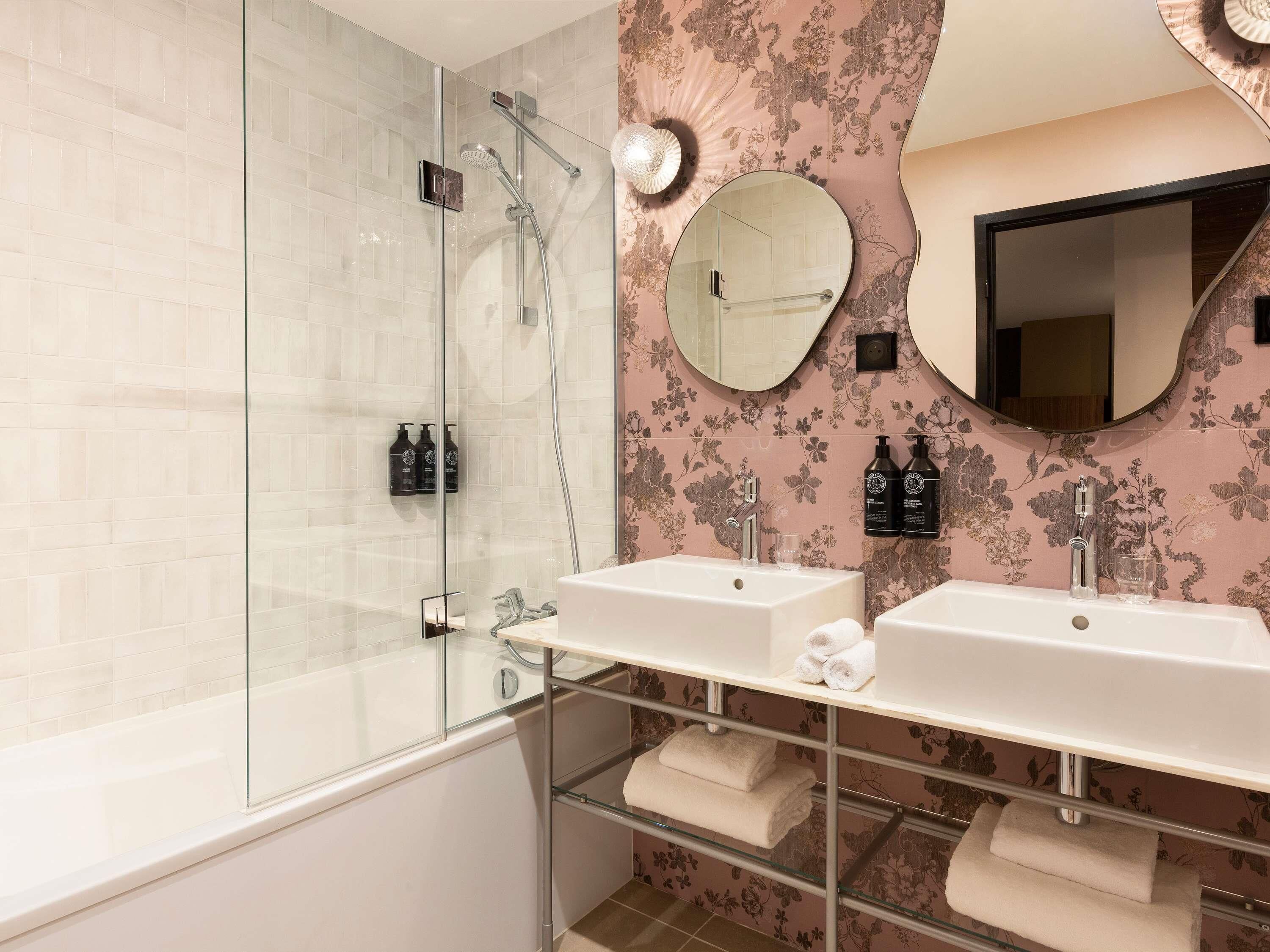 A modern bathroom with a glass-enclosed shower, two sinks, and a vanity with a mirror.