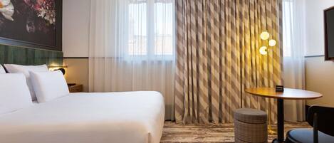 A hotel room with a large bed, a small table, a chair, a lamp, and a painting on the wall.