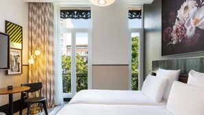 A hotel room with a large bed, a desk, a chair, and a view of the city through the window.