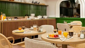 A restaurant with round tables, wicker chairs, and a green accent wall.
