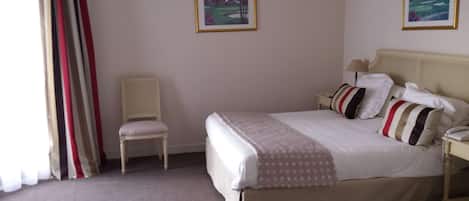 A hotel room with a bed, a chair, two framed pictures on the wall, and a lamp on the nightstand.