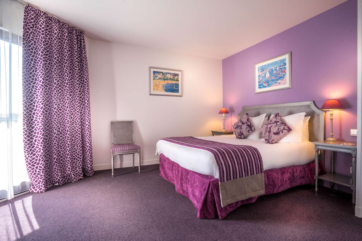 Een hotelkamer met een bed, een stoel, twee schilderijen aan de muur en een nachtkastje met een lamp.