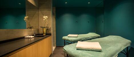 Ein Wellnessraum mit zwei Massagetischen, einer Holztheke und einem Spiegel.
