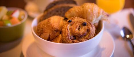 A bowl of croissants on a white plate with a cup and a glass of orange juice in the background.