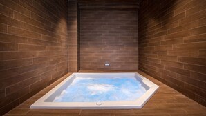 A spa room with a rectangular hot tub, wooden walls, and a control panel on the wall.
