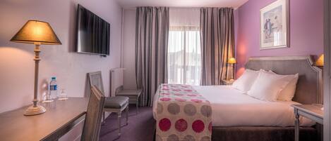 A hotel room with a bed, a desk, a chair, a TV, and a window with curtains.