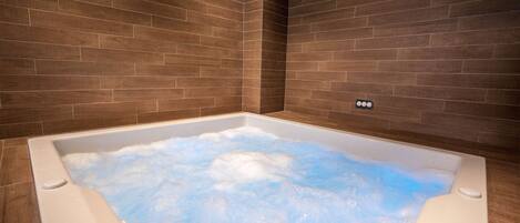 A modern bathroom with a large bathtub filled with bubbles, surrounded by dark wooden walls.