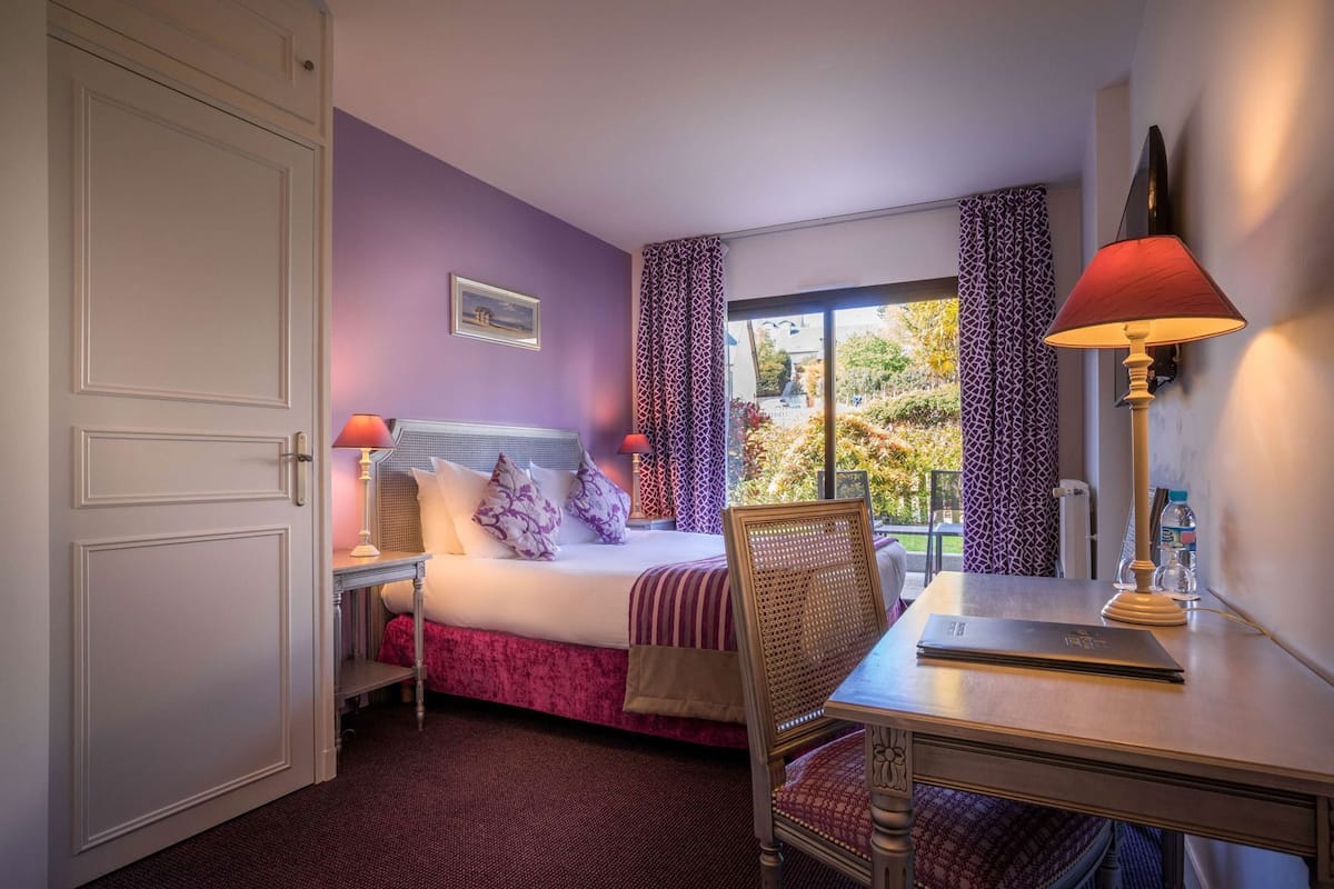 Een hotelkamer met een bed, een bureau, een stoel, een raam met gordijnen en een schilderij aan de muur.