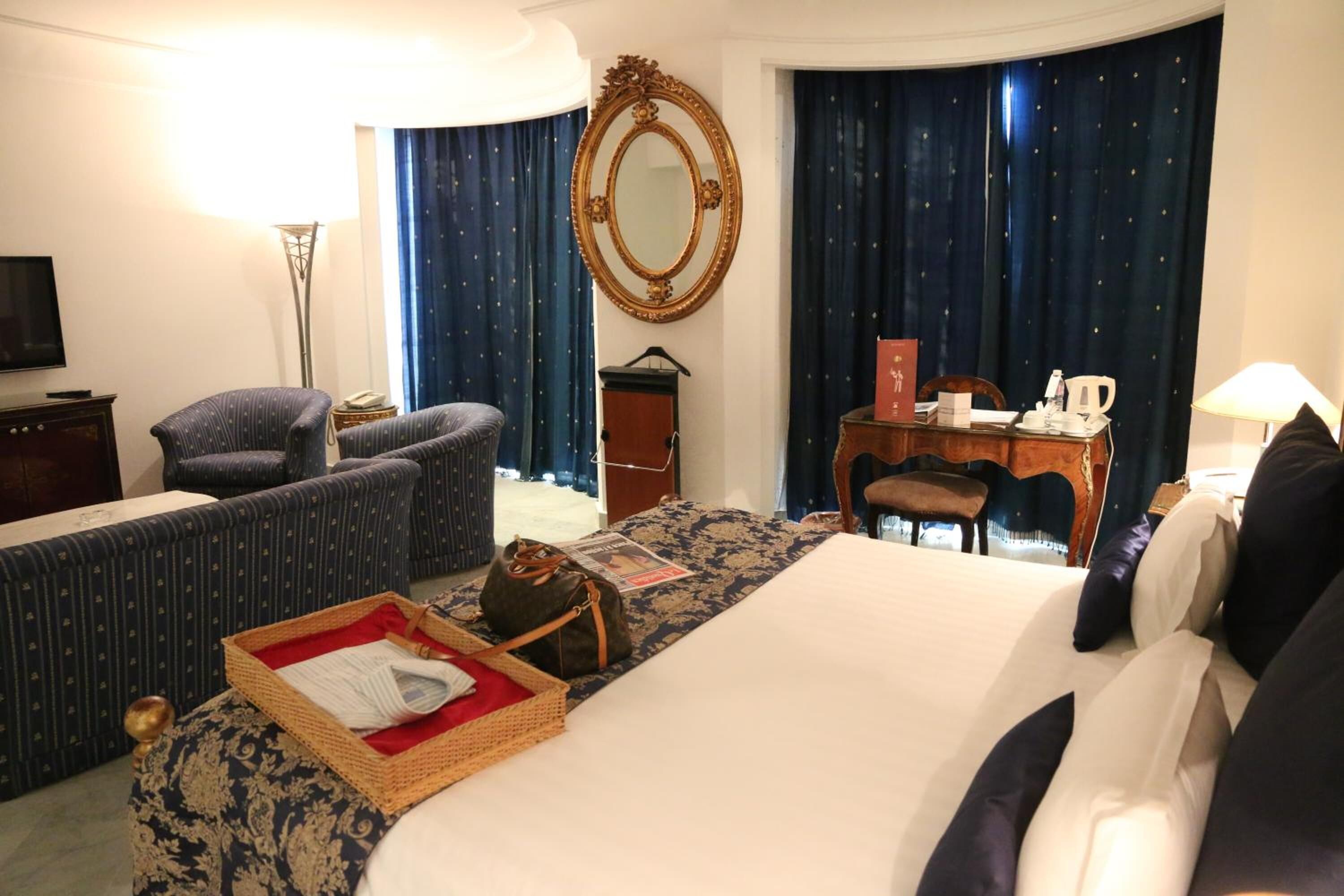 Camera d'hotel con un letto grande, un divano, una scrivania con sedia, una televisione e uno specchio.