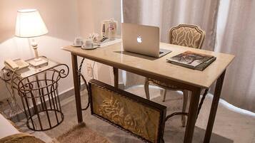 Une chambre d’hôtel avec un bureau en bois, un ordinateur portable, une lampe, un téléphone, une petite poubelle et un miroir décoratif.