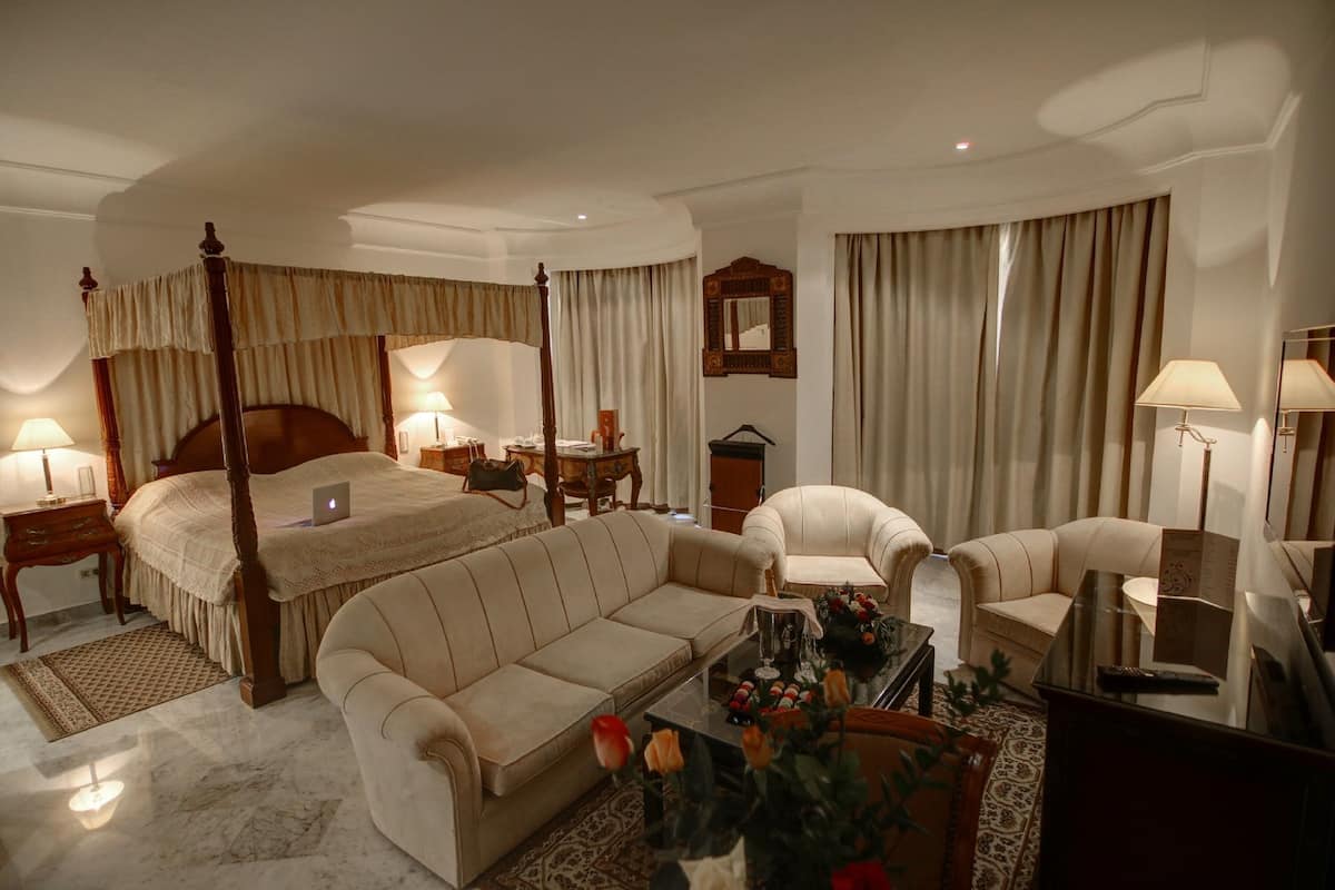 Ein geräumiges Hotelzimmer mit Himmelbett, Sofa, Sessel, Schreibtisch und Fernseher.