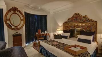 Una habitación de hotel con una cama grande, un espejo redondo, una mesita de noche, un escritorio y una silla.