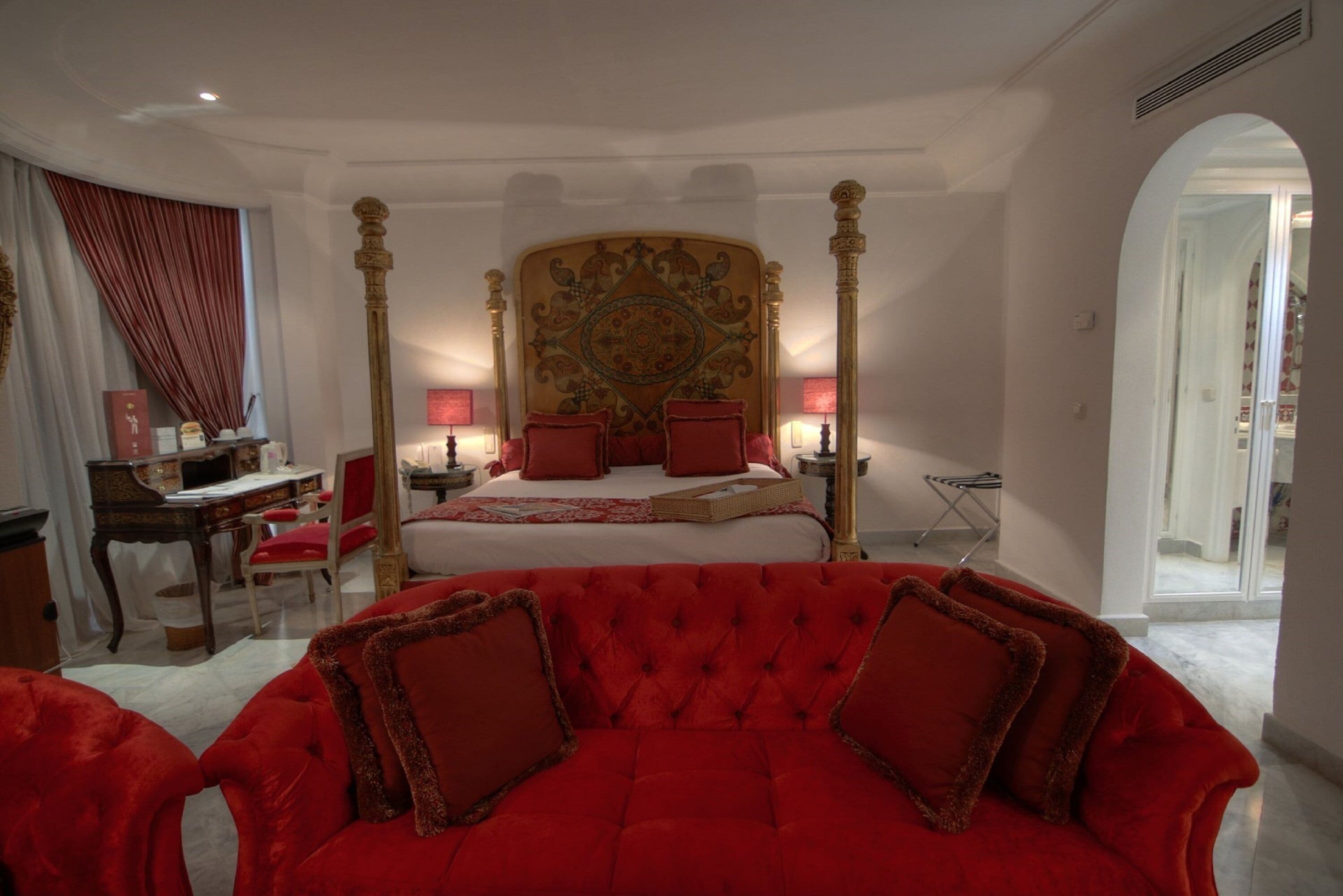 Un dormitorio con cama con dosel, un sofá tapizado rojo y un escritorio con silla.