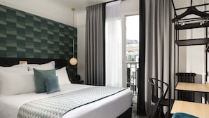 A hotel room with a bed, a desk, a chair, and a view of the city. - Maison 46 (Paris)