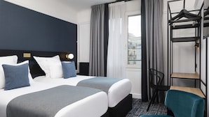 A hotel room with two beds, a desk, a chair, and a hanging rack. - Maison 46 (Paris)