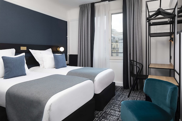 Habitación de hotel con dos camas, un escritorio, una silla y un perchero.