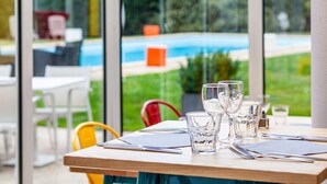 Une table à manger donnant sur une piscine, grâce à de grandes fenêtres.