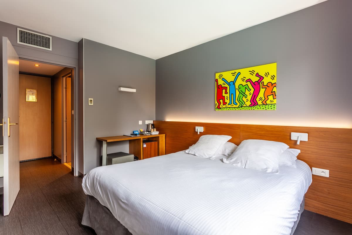 A hotel room with a bed, bedside table, and a colorful artwork on the wall.