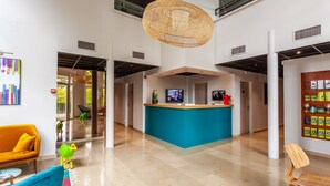 Un hall d’entrée spacieux avec un comptoir d’accueil central, un canapé jaune vif et un tapis aux couleurs vives.